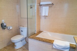 Un baño con inodoro, cabina de ducha de vidrio y bañera con una toalla a un lado.