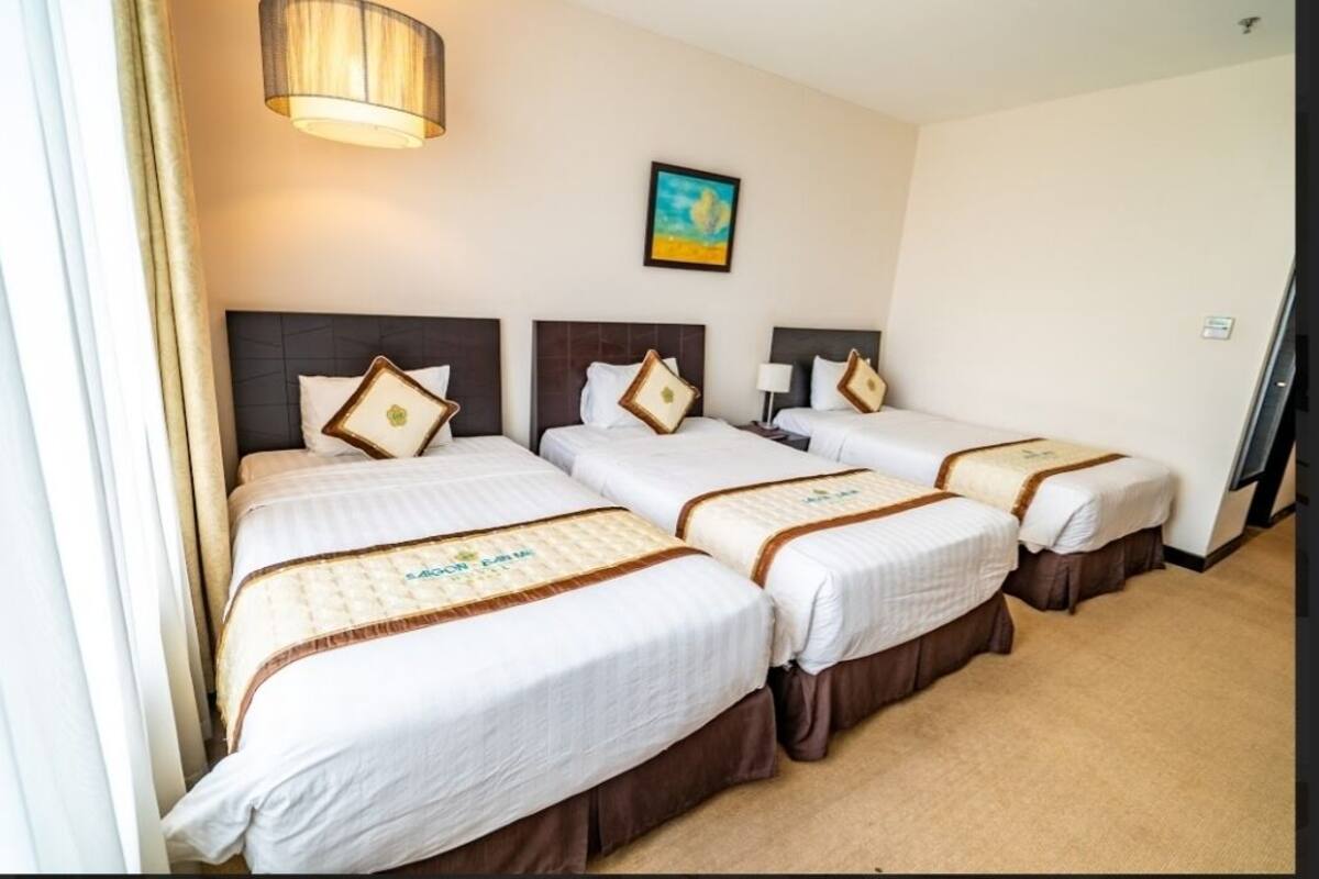 Une chambre d’hôtel avec trois lits, chacun doté d’une tête de lit, d’une table de chevet et d’une lampe.