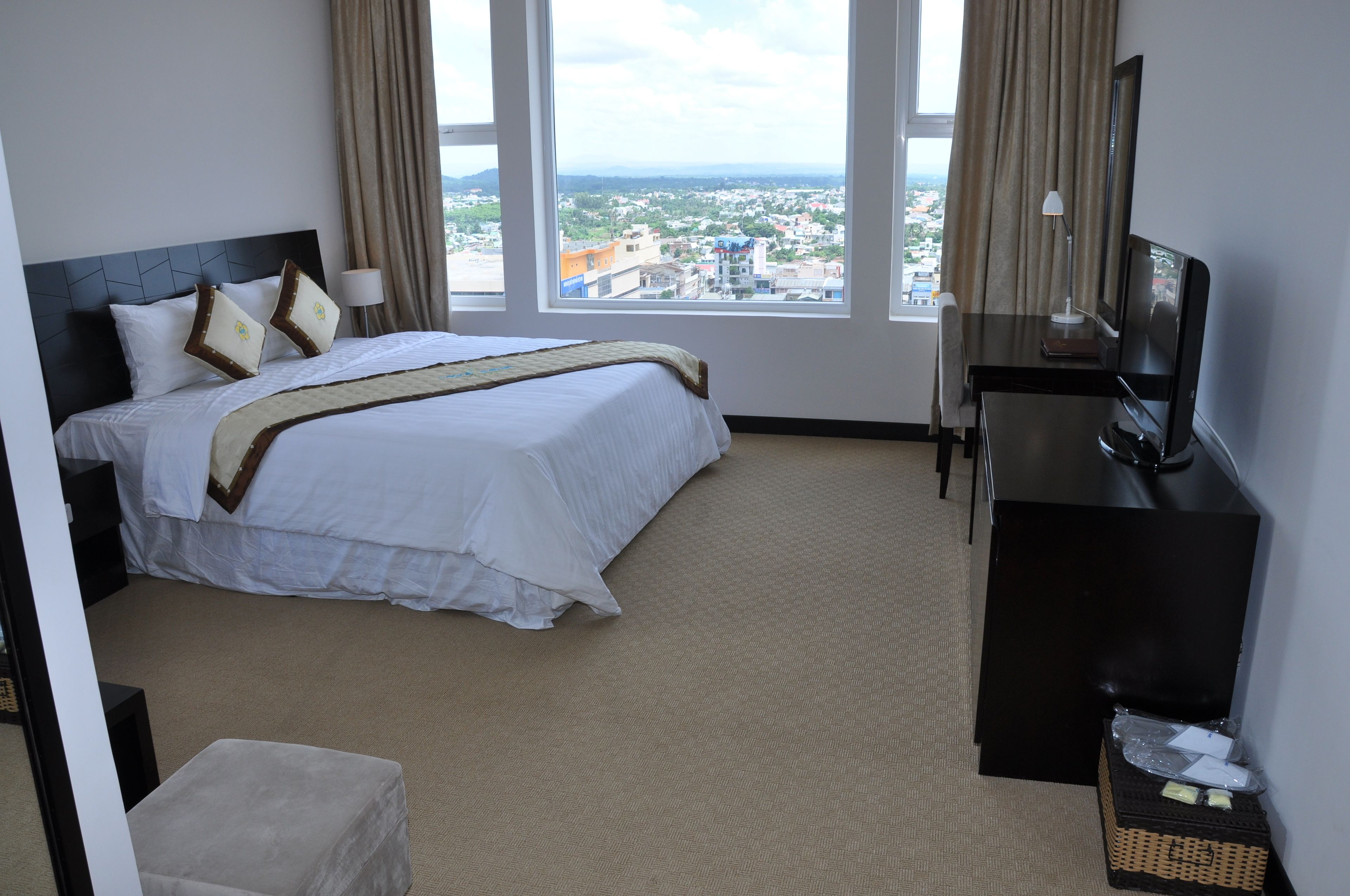 Een hotelkamer met een bed, een bureau, een televisie en uitzicht op de stad.