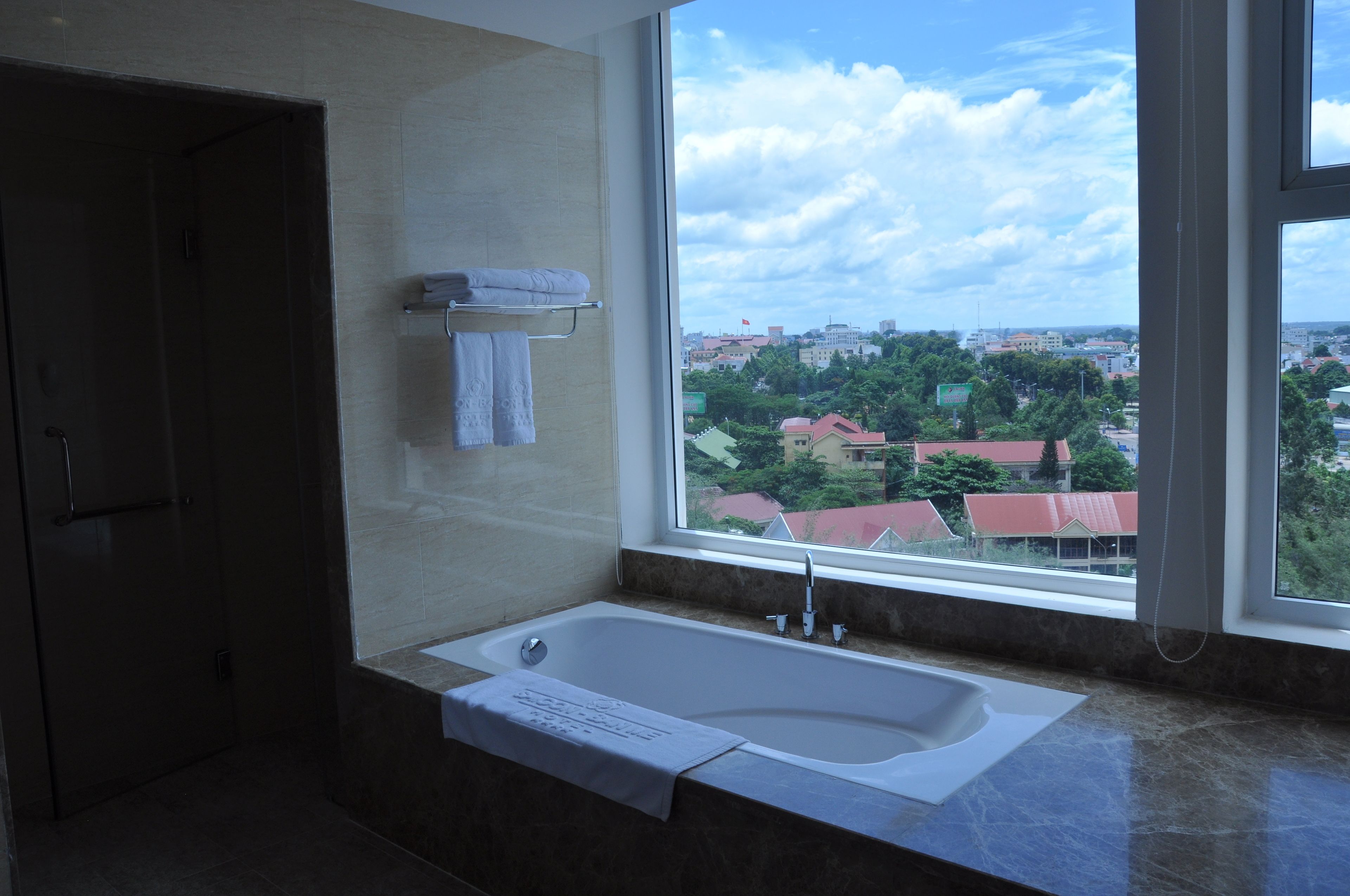 A modern bathroom with a large bathtub, a towel rack, and a window offering a city view.
