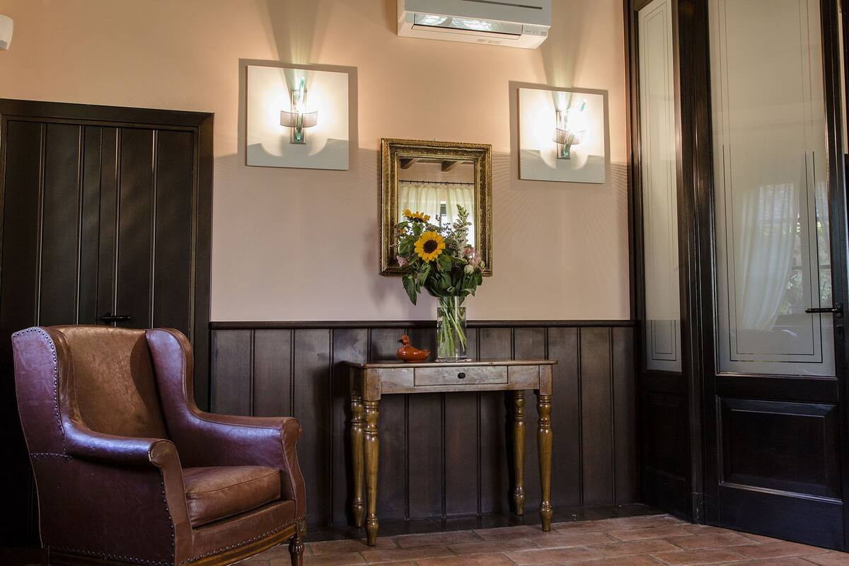 A brown leather chair, a wooden console table with a vase of flowers, and a mirror on the wall.