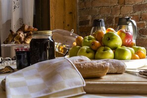 A table with a checkered cloth, a jar of jam, a plate of apples and oranges, a loaf of bread, and a coffee maker. - La Locanda di Sant'Anna (Truccazzano)