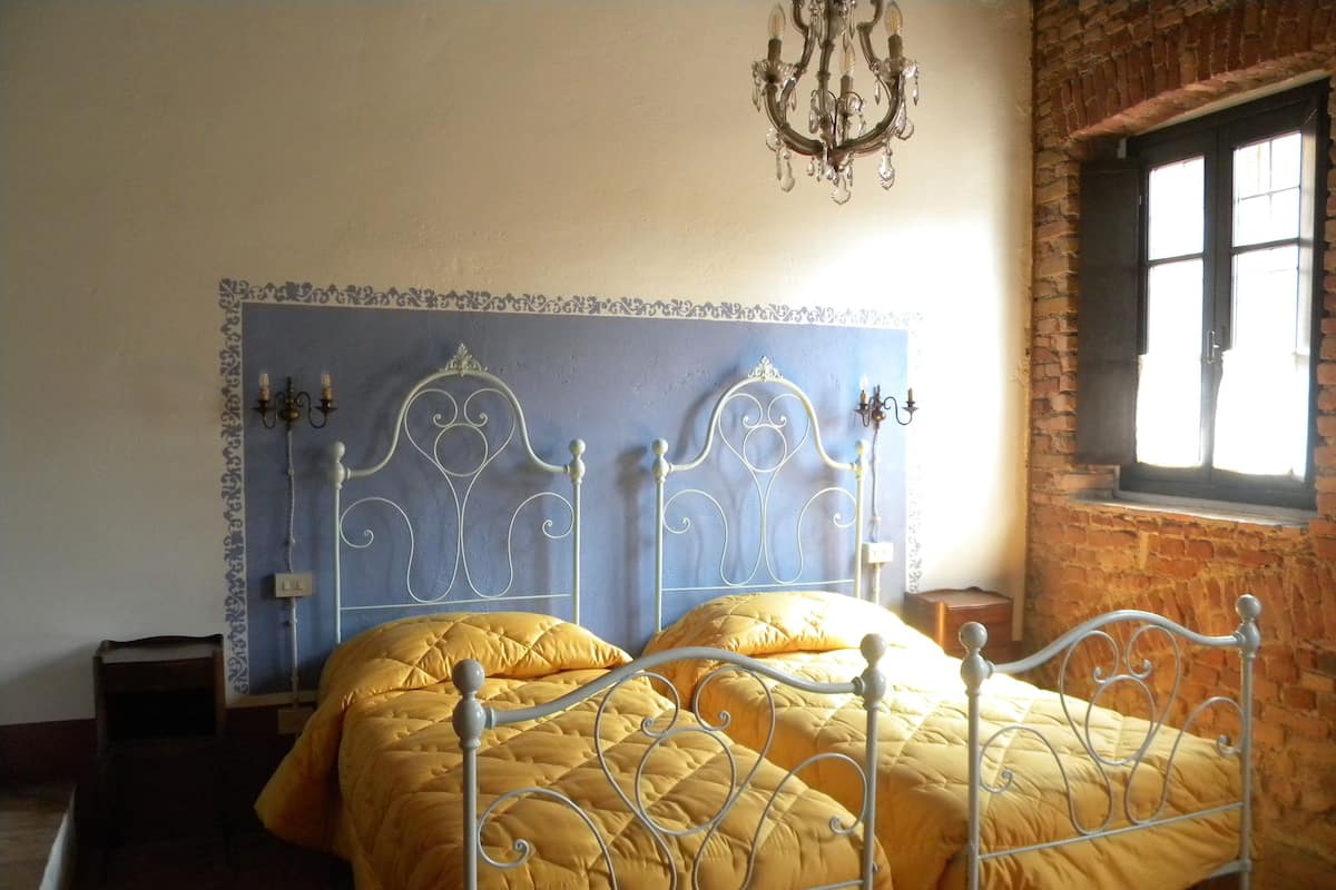 A bed with a metal frame and a yellow quilt, a chandelier, and a brick wall.