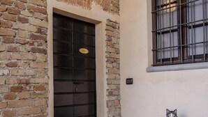 A brick exterior with a dark door, a window with metal bars, and a cat sitting on a ledge. - La Locanda di Sant'Anna (Truccazzano)