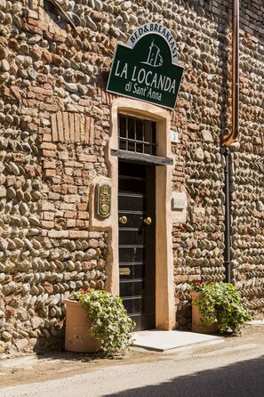 Un bâtiment en pierre avec une enseigne indiquant « LA LOCANDA di Sant'Anna » et une porte noire.