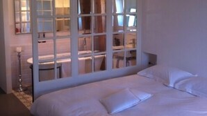 A hotel room with a large bed, a desk with a chair, and a mirror. - L'Hôtel Particulier (Nancy)