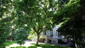 A building with a central staircase, surrounded by lush green trees and grass. - L'Hôtel Particulier (Nancy)
