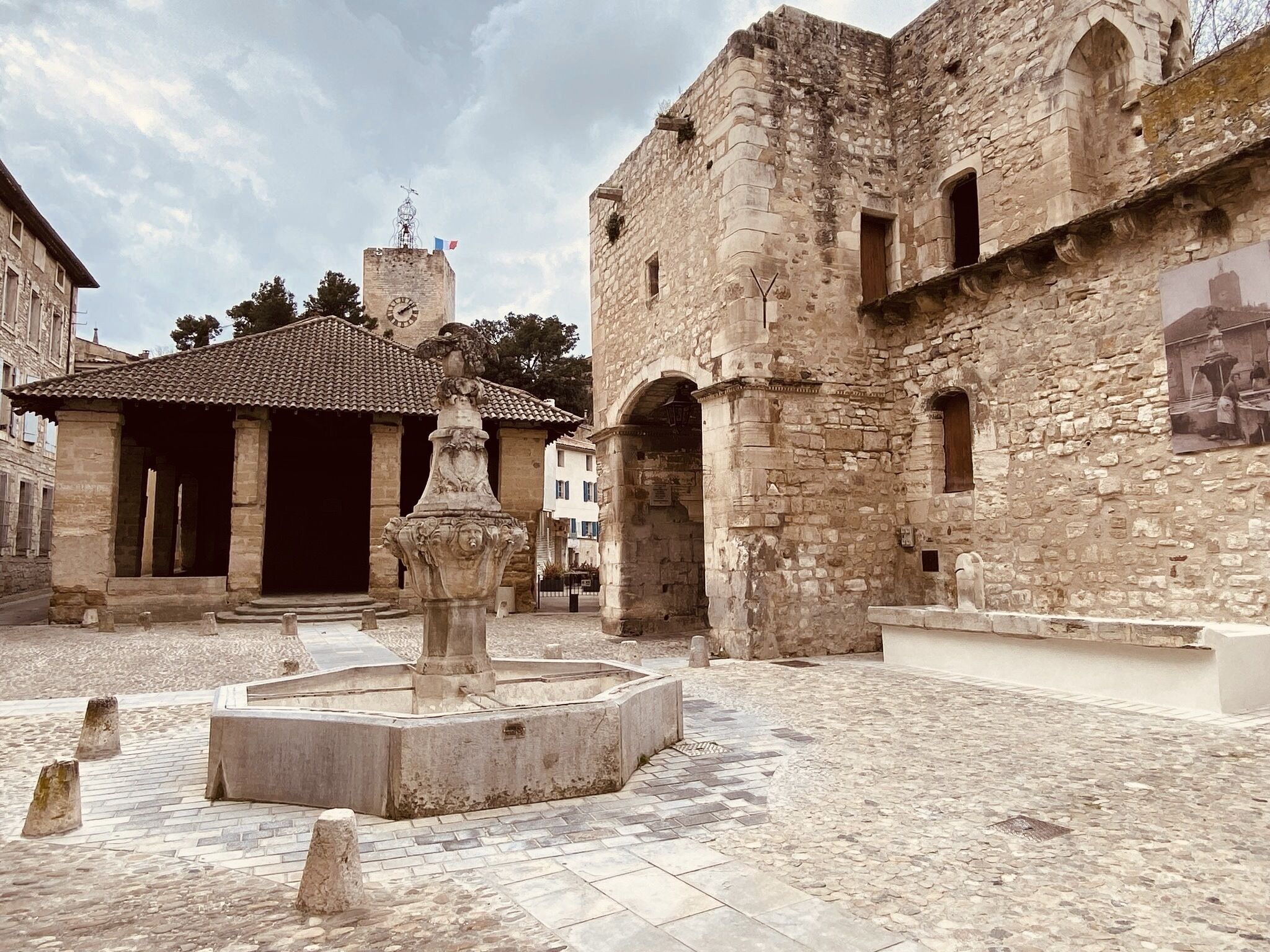Une cour avec une fontaine, des bâtiments en pierre et une toiture en tuiles.