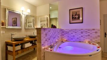 A modern bathroom with a large bathtub, two sinks, and a vanity with storage.