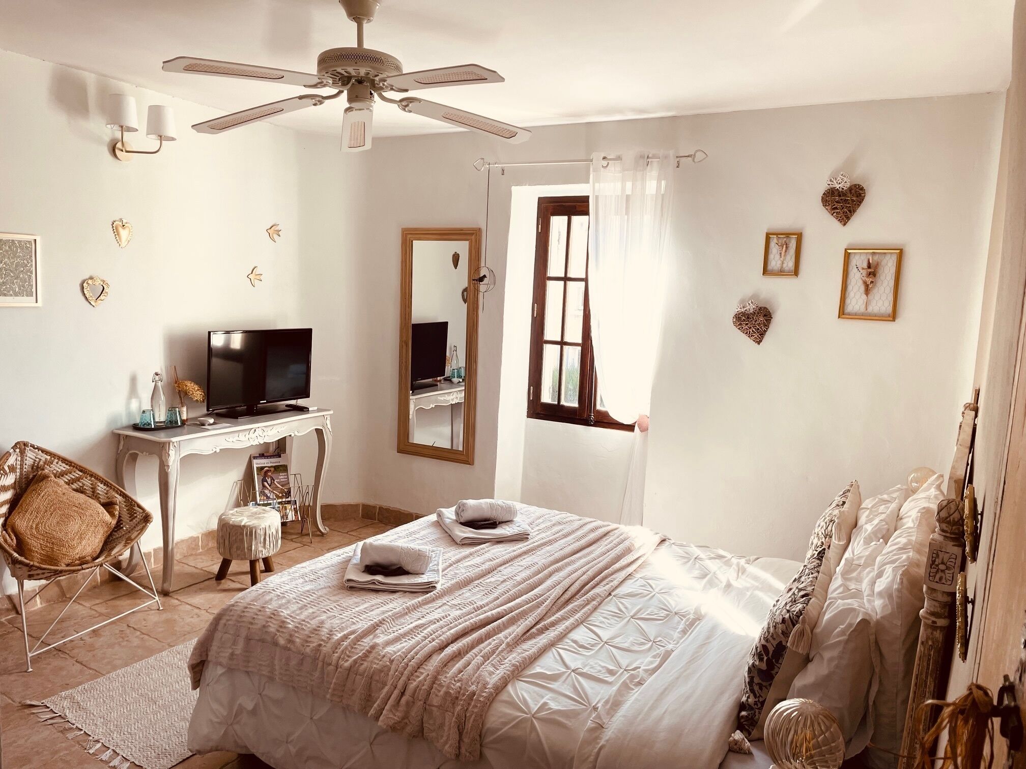Un dormitorio con cama, escritorio con televisor, silla, ventilador de techo y decoración en la pared.