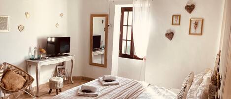 Un dormitorio con cama, escritorio con televisor, silla, ventilador de techo y decoración en la pared.