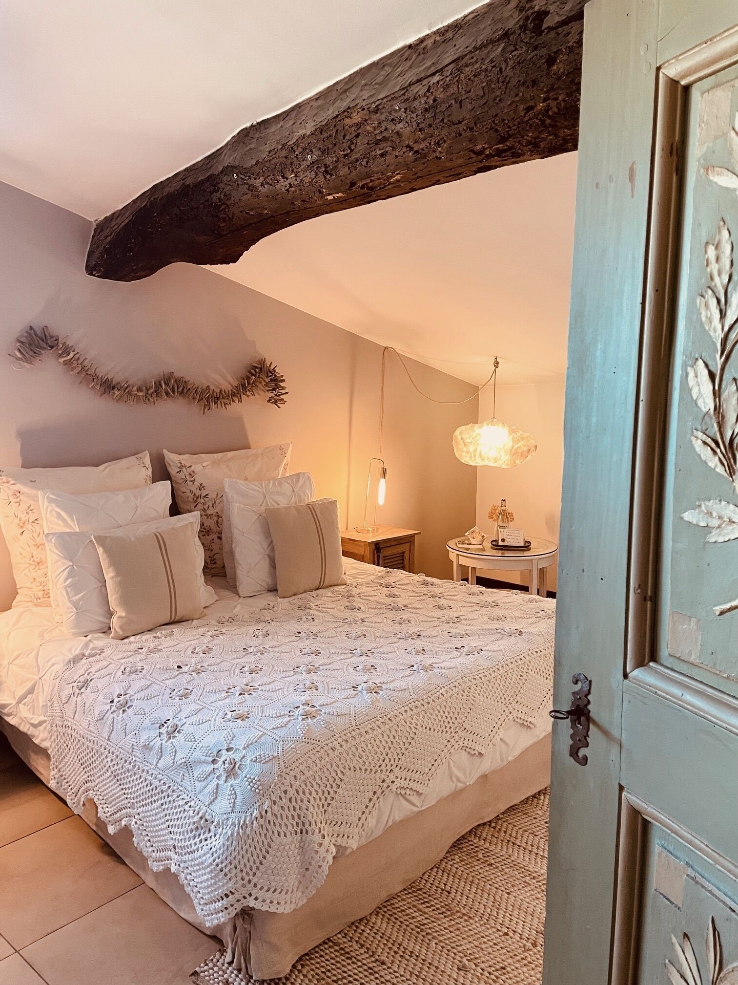 A cozy bedroom with a large bed, a wooden ceiling beam, and a decorative wall hanging.