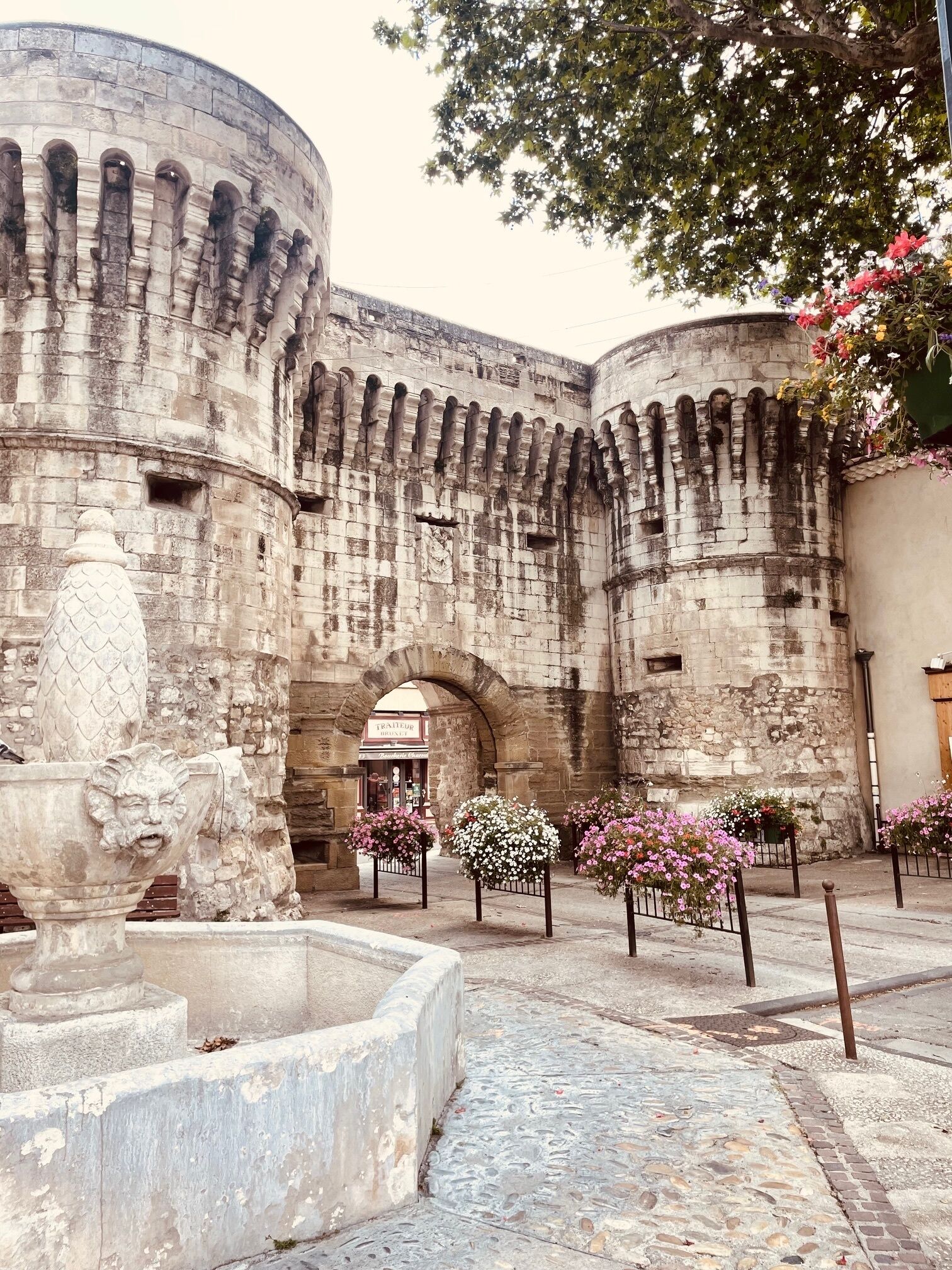 Un edificio de piedra histórico con una torre redonda, una fuente y arreglos florales.