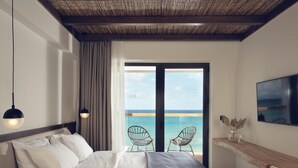 Une chambre avec un lit, une télévision, une vue sur la mer et un balcon avec des chaises.
