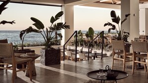 Un espace extérieur ensoleillé, aménagé avec des meubles en osier, des plantes en pot et offrant une vue sur la mer.