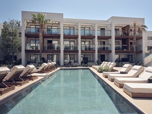 Un hotel moderno con piscina, varios balcones y sillones de descanso.