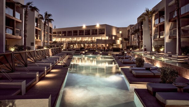 Un hôtel doté d’une piscine, d’un espace extérieur aménagé et de palmiers.