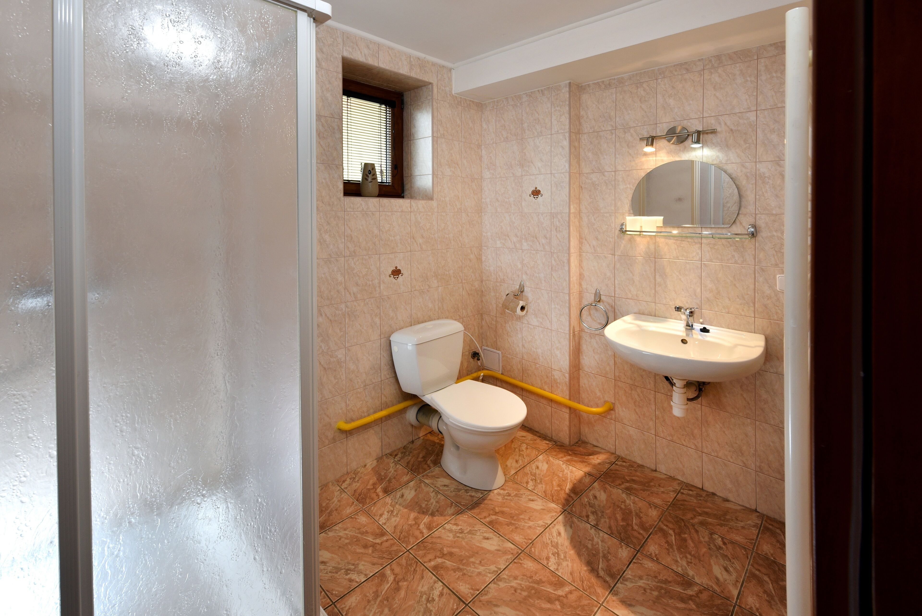 Un baño con inodoro, lavamanos y una ventana con persianas.