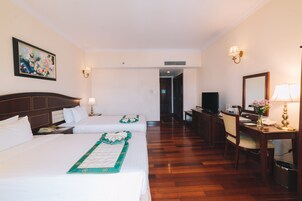 A hotel room with two beds, a desk with a computer, a chair, a TV, and a painting on the wall.