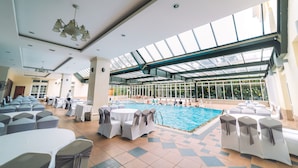 An indoor swimming pool area with a glass ceiling, surrounded by tables and chairs with white tablecloths and gray sashes. - Saigon Dalat Hotel (Xuan Huong - Da Lat)