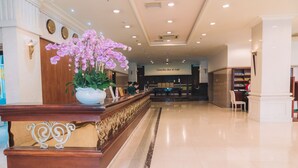 A reception area with a marble floor, a reception desk, a large potted orchid, and a sign for Camellia Bar & Cafe in the background. - Saigon Dalat Hotel (Xuan Huong - Da Lat)