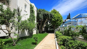 Caminho ladeado por vegetação e um edifício branco com telhado azul.