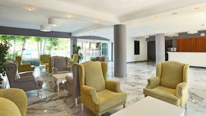 Um hall amplo com várias áreas de estar, um balcão de recepção e grandes janelas que oferecem vista para o exterior.