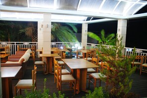 An outdoor dining area with wooden tables and chairs, surrounded by a white railing.