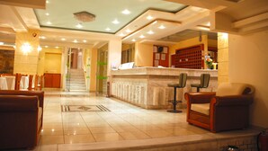 Vestíbulo de hotel con mostrador de recepción, zona de estar y una escalera que conduce a otro piso.