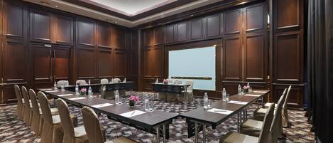 A conference room with a long table, chairs, and a large screen.
