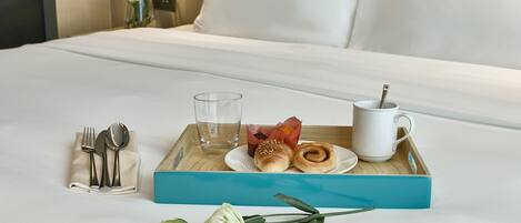 A neatly arranged breakfast tray on a bed with a white pillow and a vase of flowers in the background.