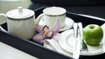 Una bandeja con tetera, taza, orquídea, manzana y cubiertos.