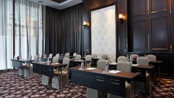 A conference room with a dark wood panel wall, large windows with sheer curtains, and a patterned carpet.