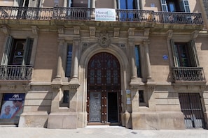 A historic building with ornate iron balconies, a central entrance with a decorative door, and a sign for 'Hostal in Barcelona'. - Hostalin Barcelona Gran Via (Barcelona)