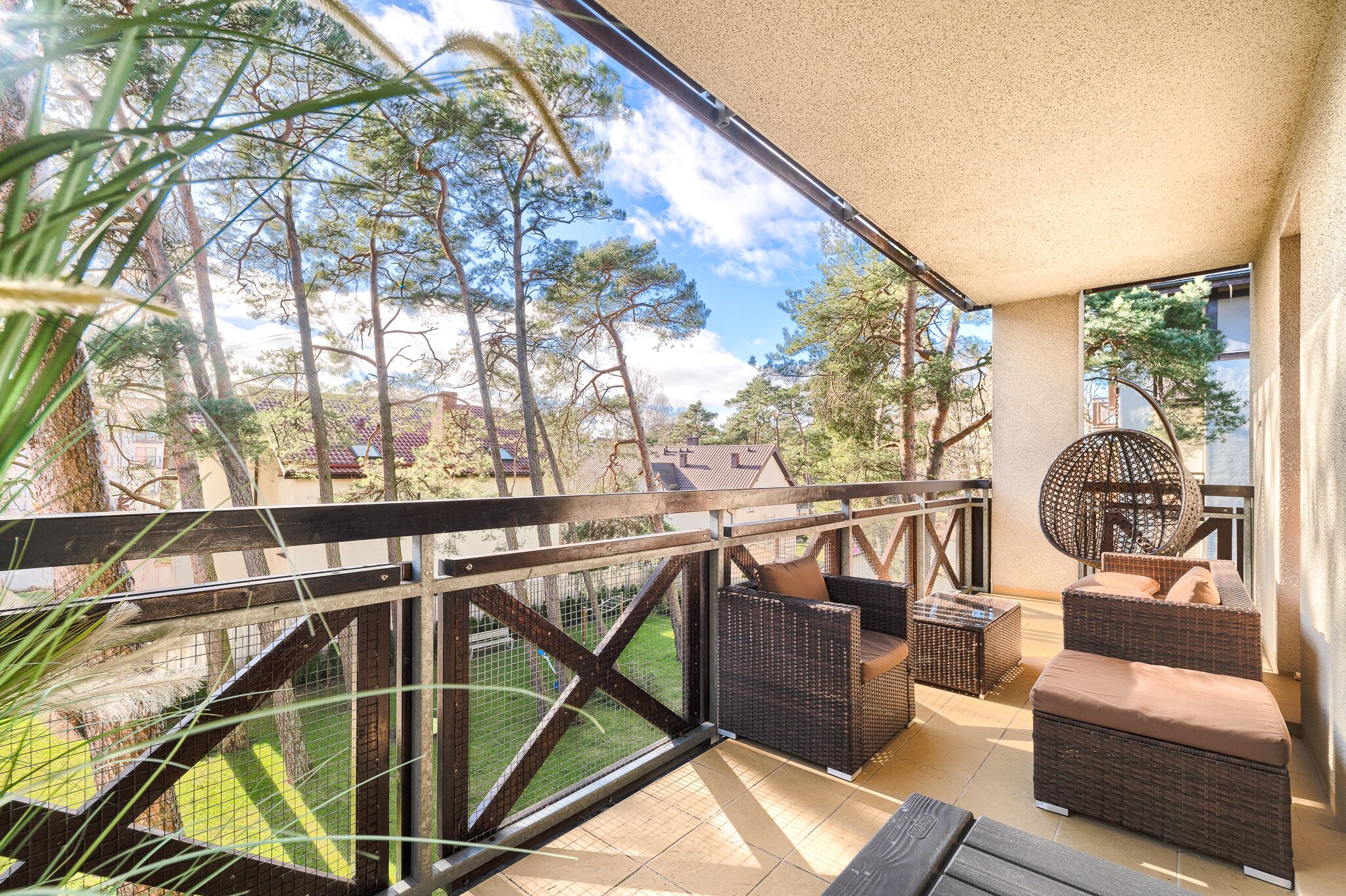 A balcony with wicker furniture, a glass railing, and a view of trees and buildings.
