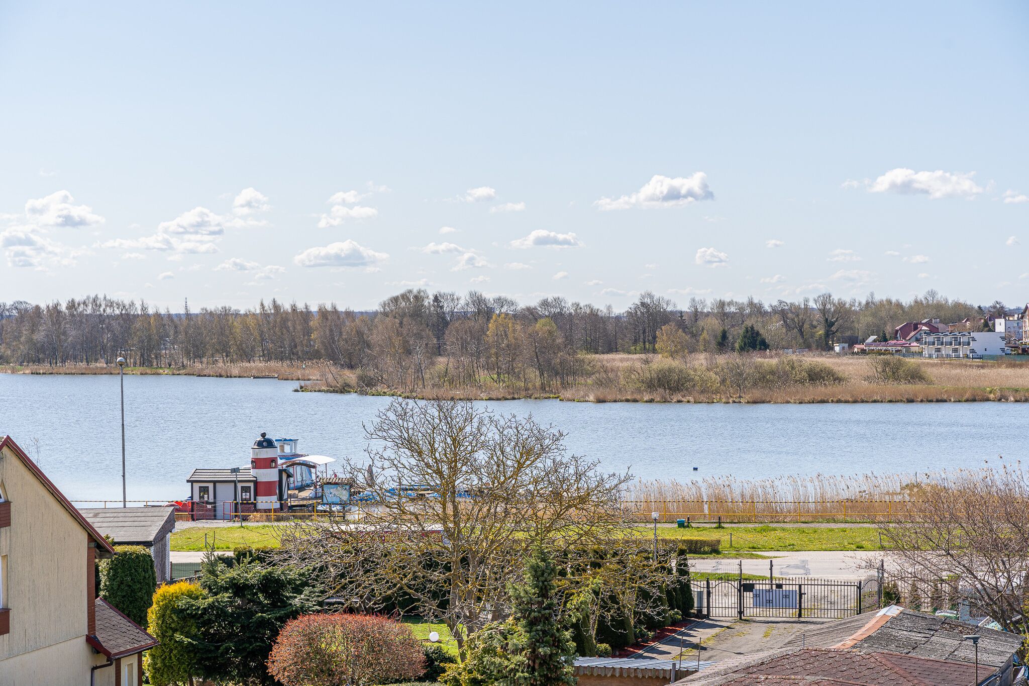 Vista del lago con un faro, un muelle y edificios residenciales.