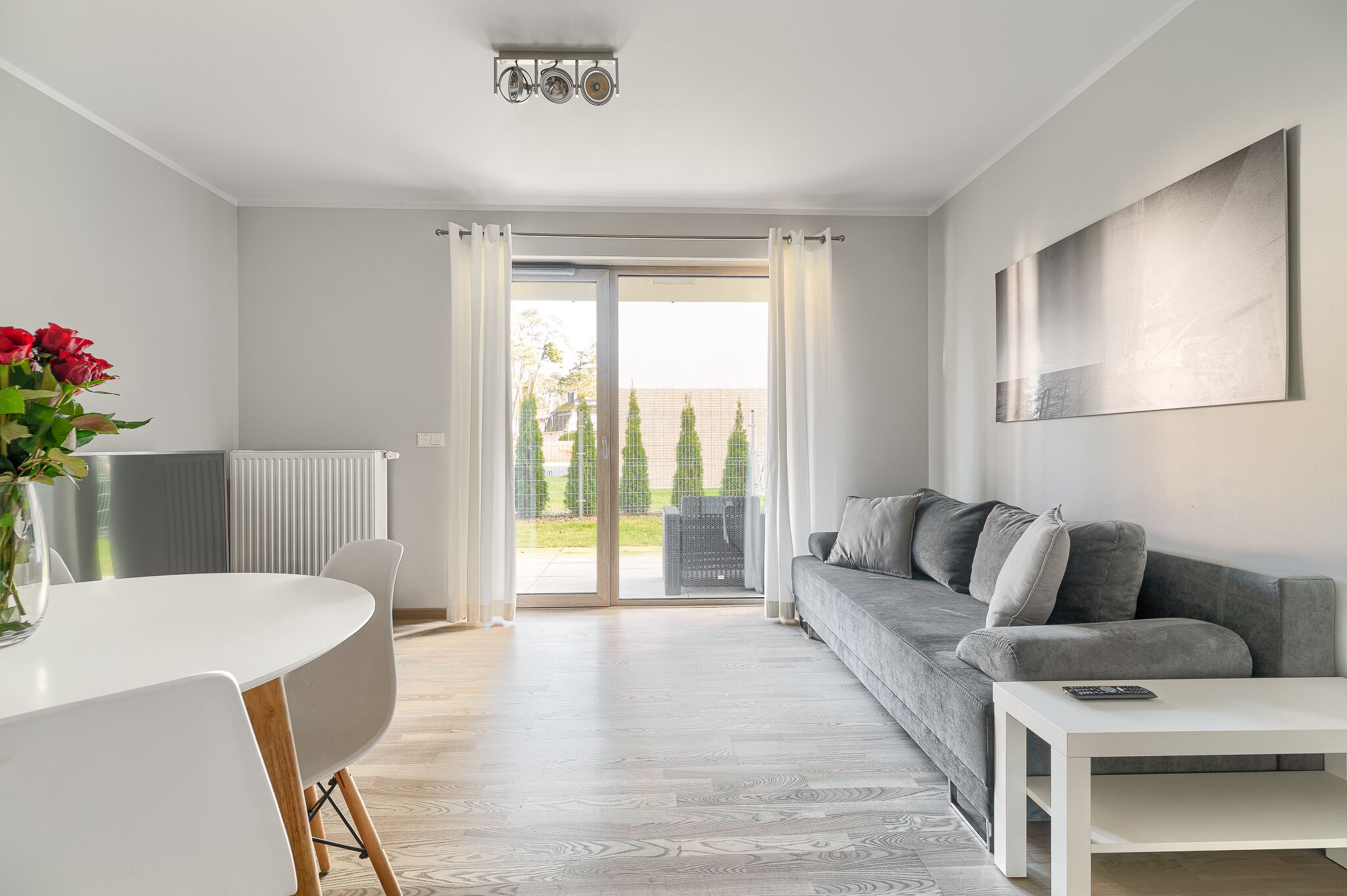 A modern living room with a grey sofa, white coffee table, and a dining area with a white table and chairs.