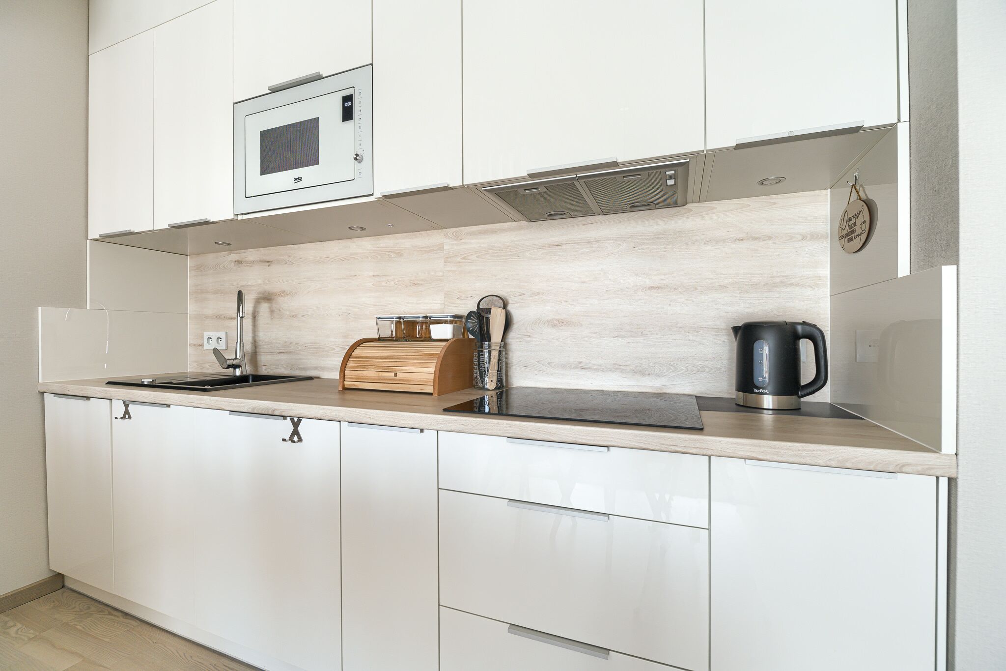 Une cuisine moderne avec des meubles blancs, un plan de travail en bois, un four à micro-ondes encastré, une bouilloire et un grille-pain.