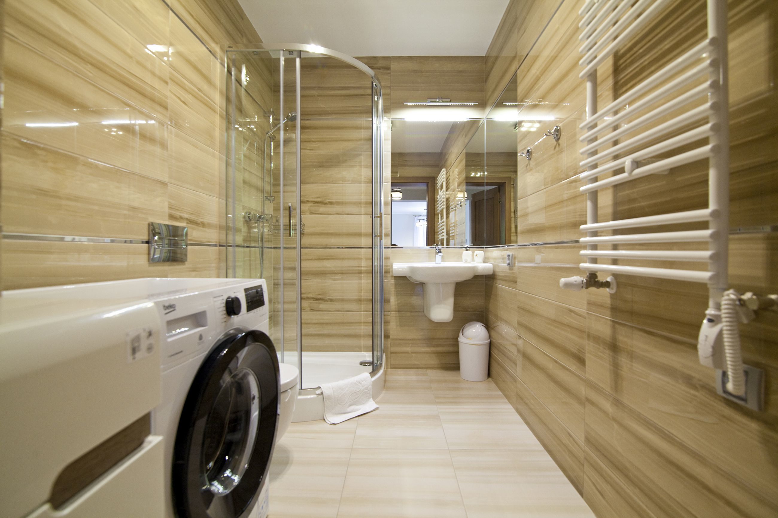 Een moderne badkamer met een glazen douchecabine, een ingebouwde wasmachine en een wastafel met handdoekhouder.
