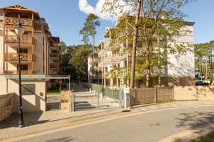 Un hotel de varios pisos con balcones, entrada vigilada y camino de acceso pavimentado.