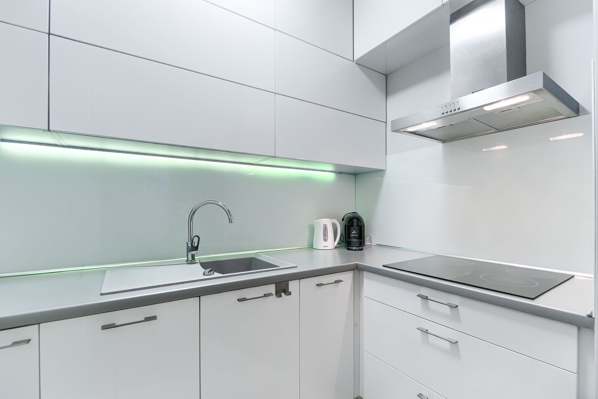 Una cocina moderna con armarios blancos, un lavamanos de acero inoxidable y una campana extractora empotrada.