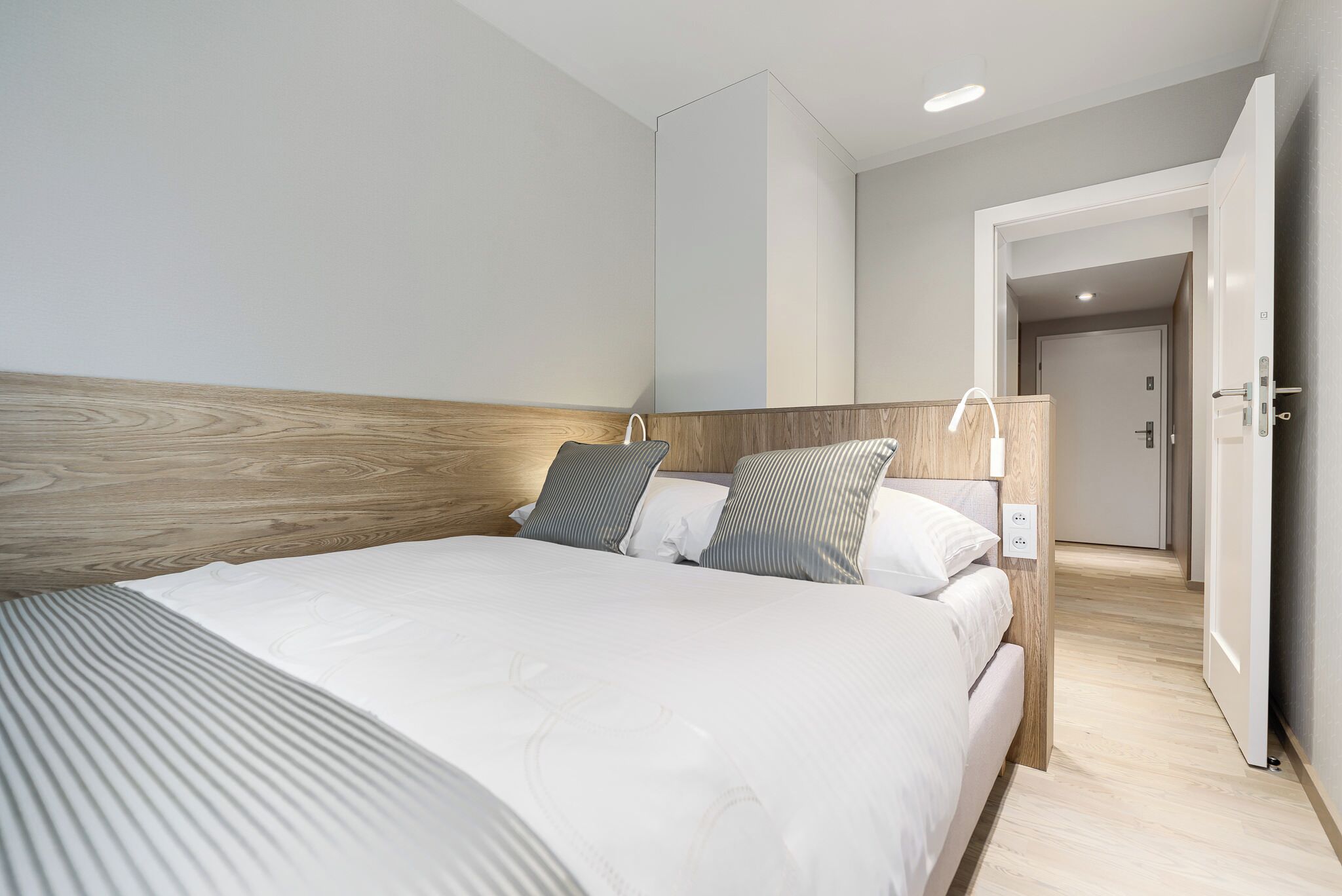 A modern hotel room with a large bed, wooden headboard, and a walk-in closet.