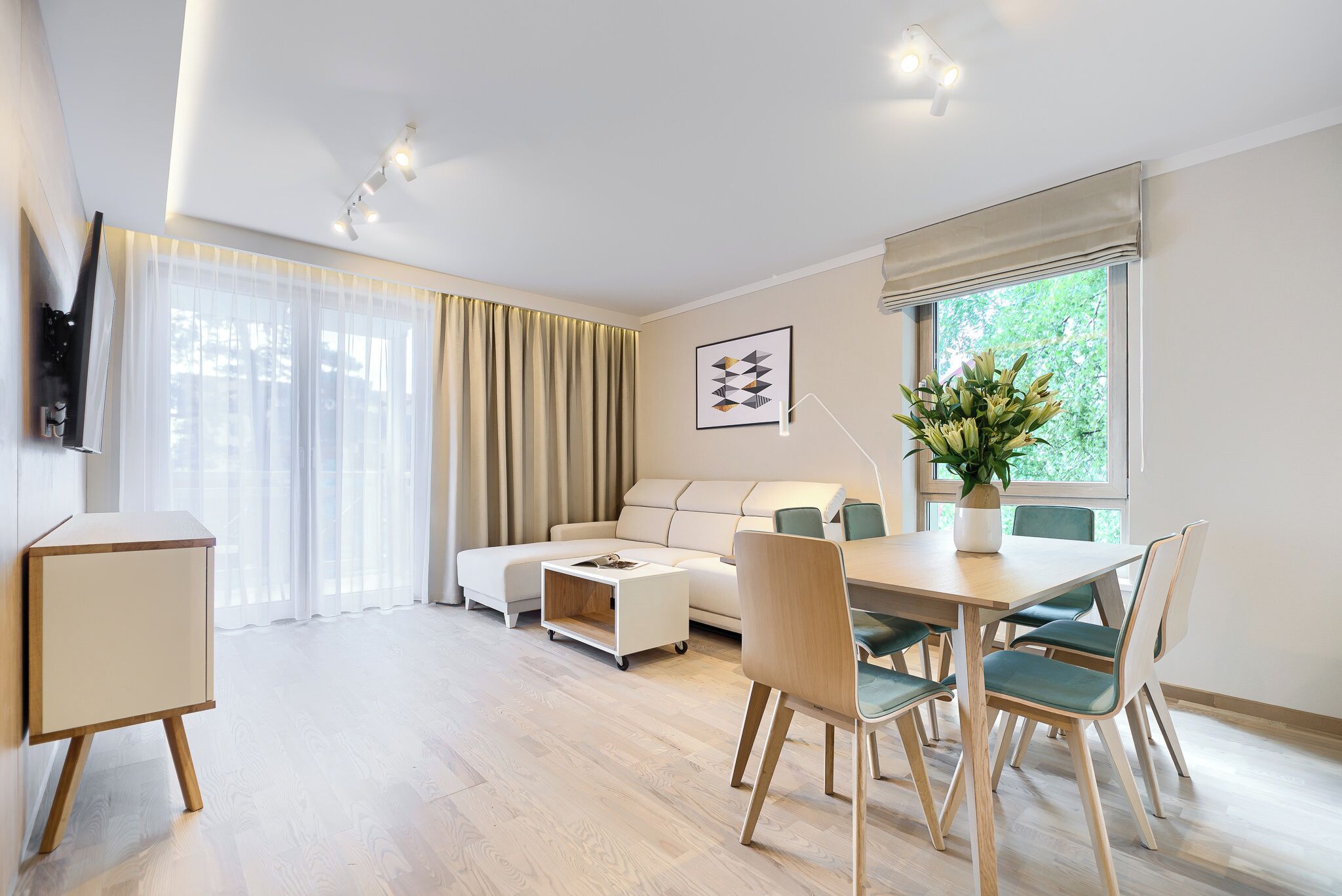 A modern living room with a sofa, dining table, chairs, and a TV mounted on the wall.