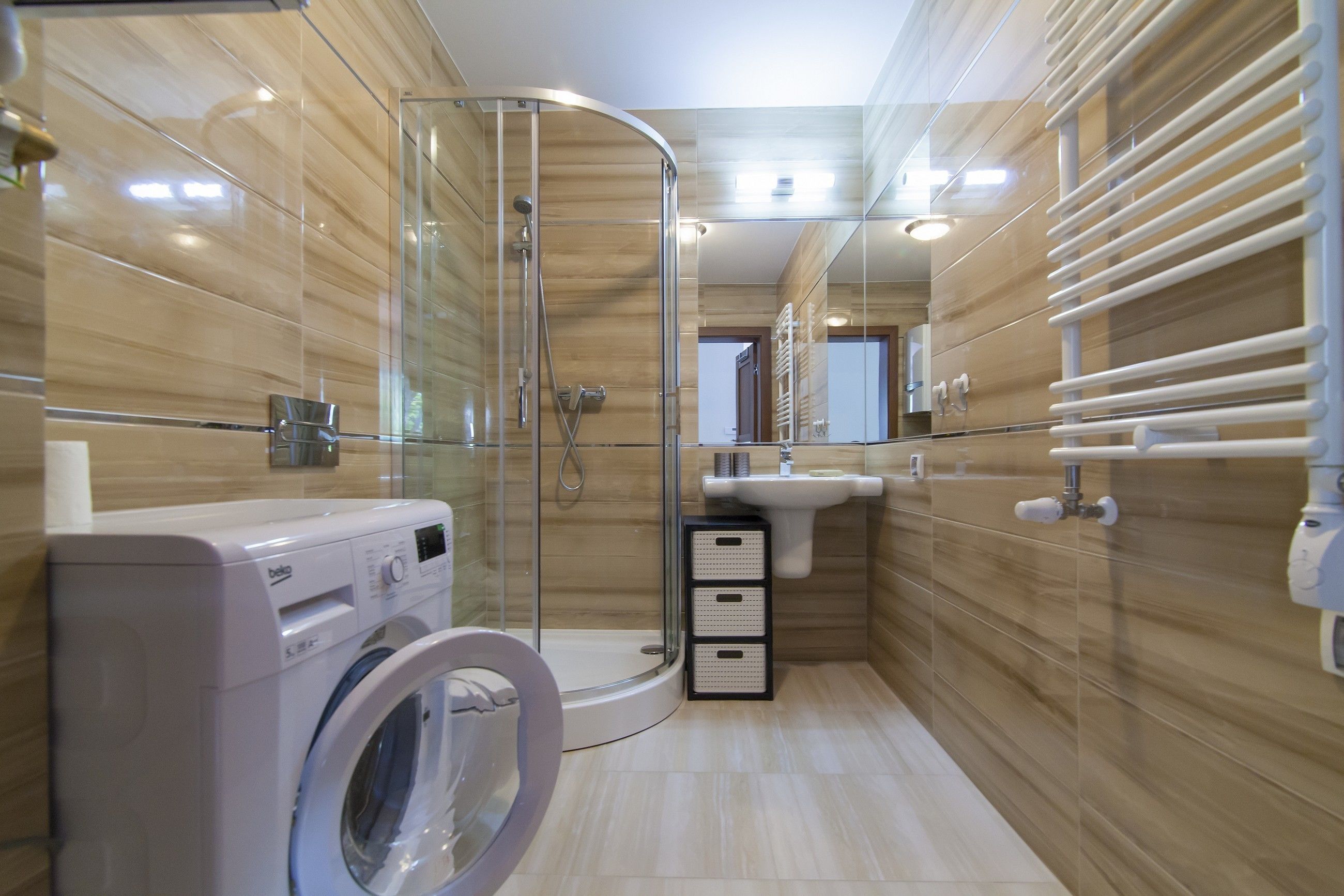 A modern bathroom with a glass-enclosed shower, a washing machine, and a sink with a mirror.