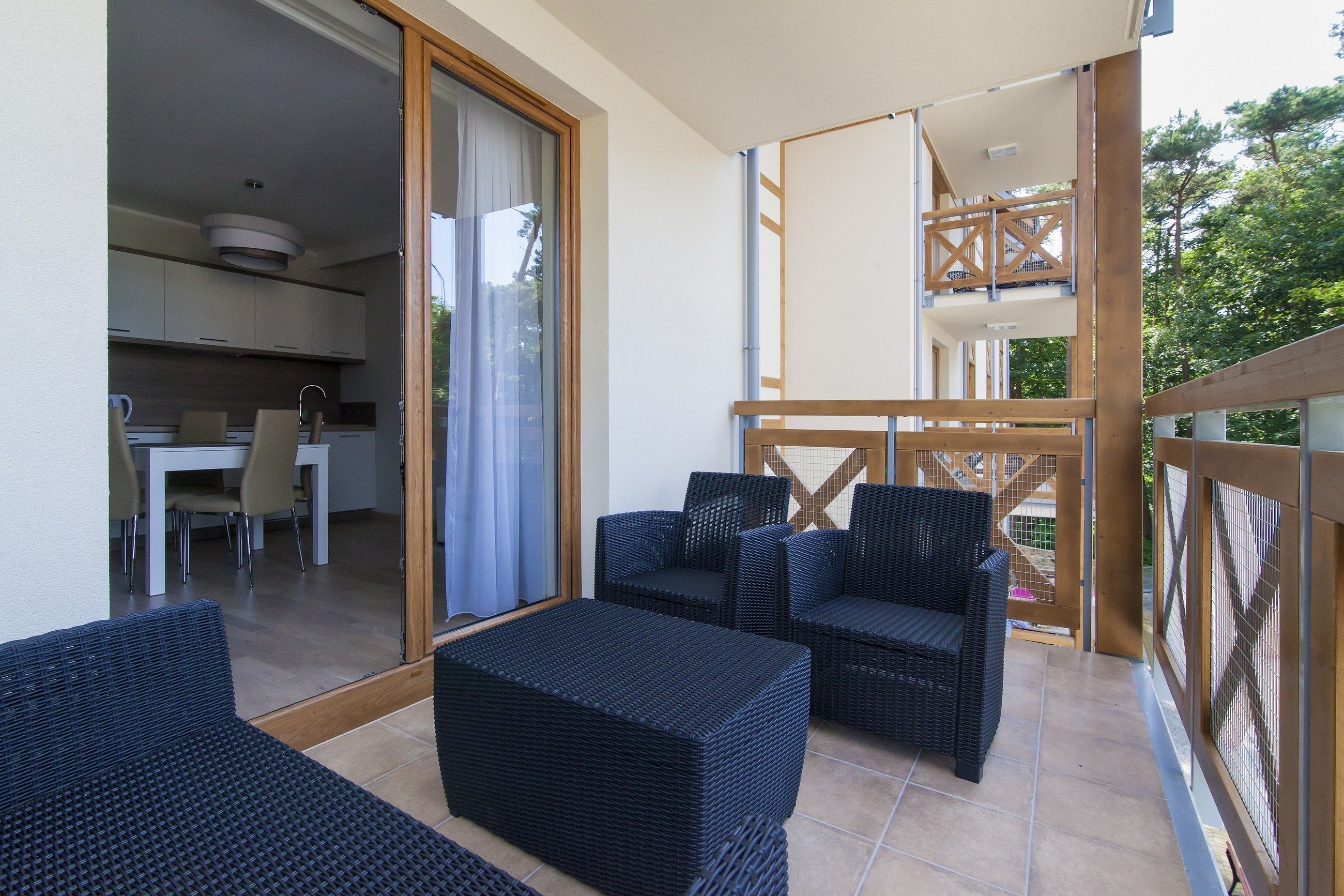 A balcony with wicker furniture, a sliding glass door leading to a kitchen, and a wooden deck.