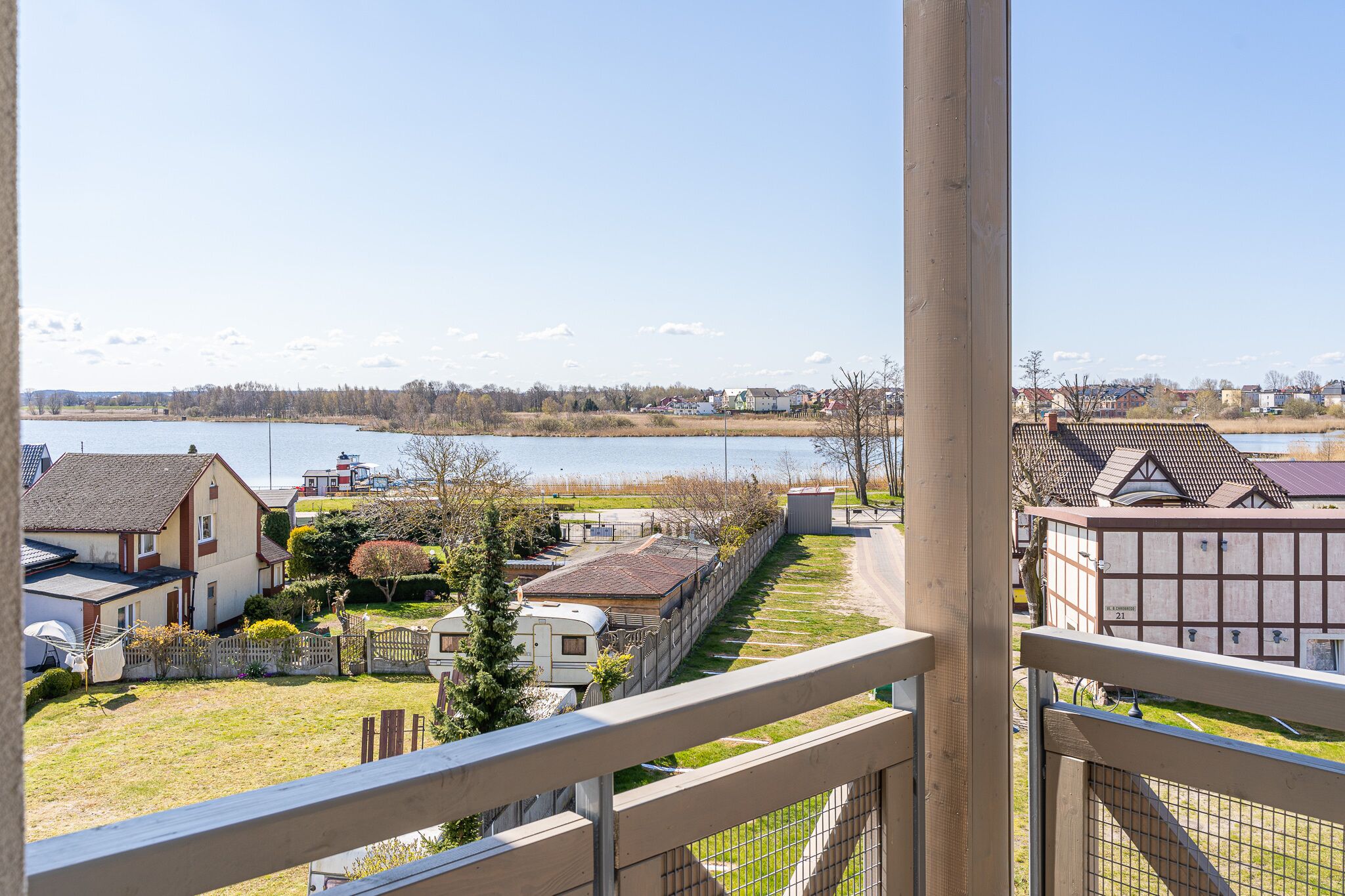 Udsigt over en sø fra en balkon med huse, en båd og et indhegnet område.