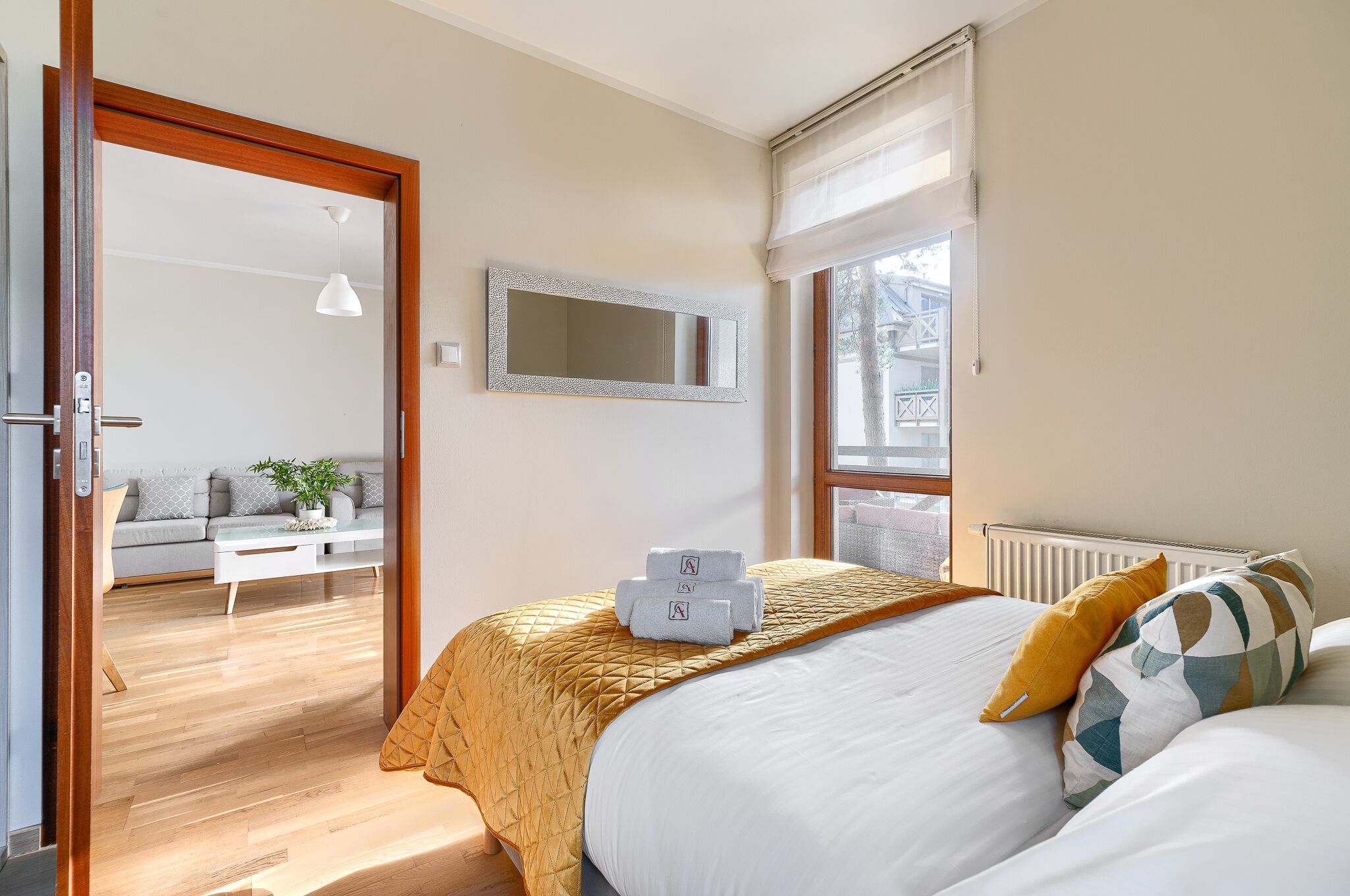 Habitación de hotel con cama, sofá, espejo y ventana con vistas al exterior.