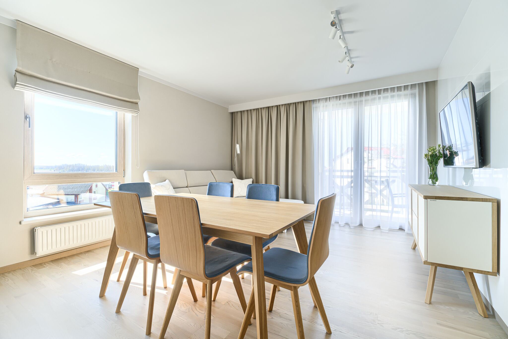 A modern dining area with a wooden table and blue chairs, a sofa, and a TV on a cabinet.