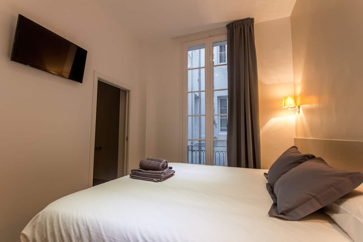 Een hotelkamer met een bed, een flatscreen televisie aan de muur, een raam met gordijnen en een wandlamp.