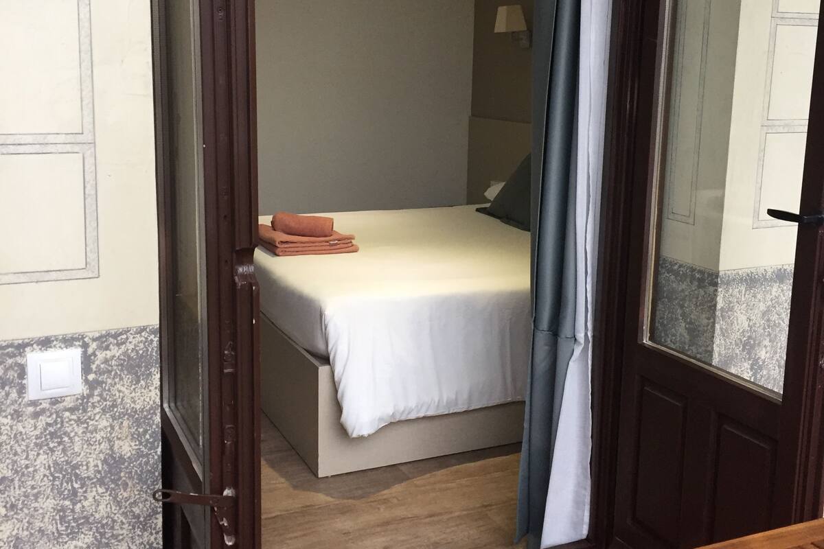 Een hotelkamer met een bed, een houten bankje en een deur die naar buiten leidt.